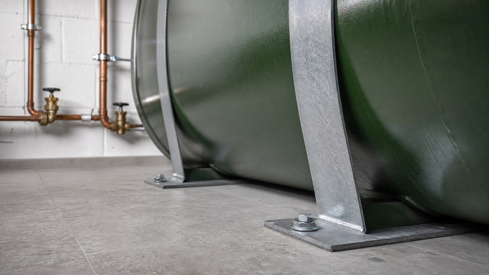 Grüner Heizöltank im Keller, mit verzinkten Stahlbändern auf verschraubten Fußplatten gegen Aufschwimmen verankert